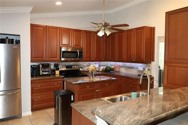 Kitchen featuring stainless steel appliances, dark stone countertops, crown molding, tasteful backsplash, and light tile patterned floors