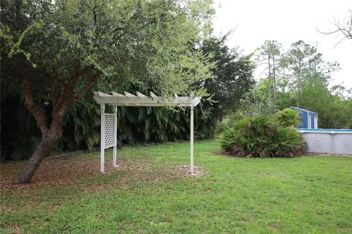 View of green lawn with a pergola, an outdoor pool, view of scattered trees, and an outbuilding