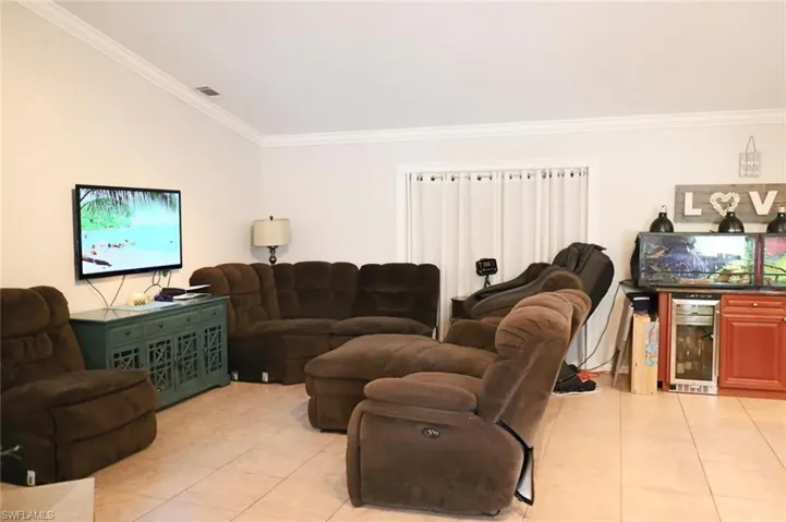 Living area featuring crown molding, light tile patterned floors, and beverage cooler