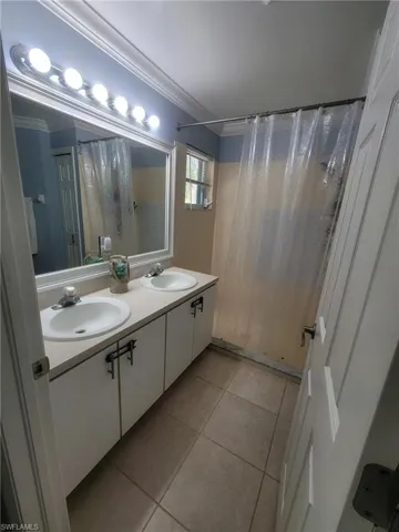 Bathroom featuring double vanity, light tile patterned floors, and crown molding