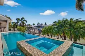 Waterfront property featuring an outdoor swimming pool, integrated spa with mosaic tile surround, and lush palm trees