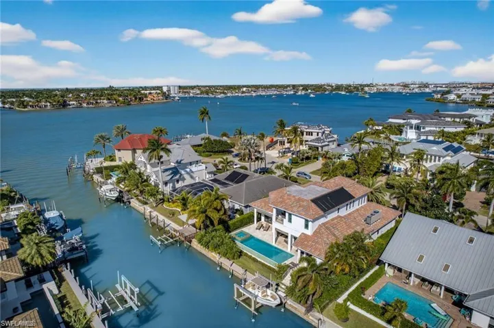 Waterfront residence featuring a private pool, multiple boat slips, mature palm trees, and a tile roof