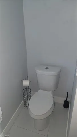 White toilet with a dual-flush mechanism, light gray wall paint, and large format floor tiling