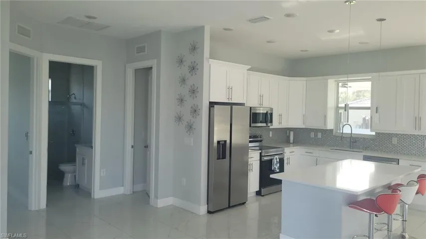 Bright kitchen featuring white shaker cabinetry, stainless steel appliances, a white island with pendant lighting, and a mosaic tile backsplash