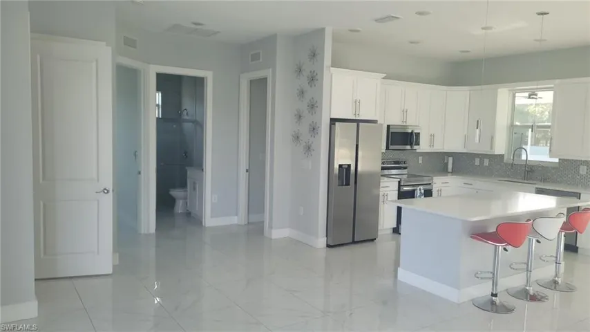 Open-concept kitchen featuring white cabinetry, stainless steel appliances, a large island with countertop seating, and a patterned tile backsplash