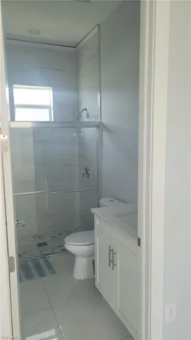 Bathroom featuring a glass-enclosed shower, white tile walls with subtle veining, a single window, a white vanity with double-door cabinetry, and a white countertop with an integrated sink