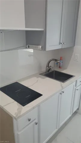 Compact kitchen area featuring white shaker-style base cabinetry, light gray upper cabinetry, and a white countertop with subtle veining