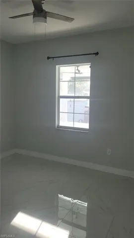 Bright room featuring a window with a curtain rod, a ceiling fan with integrated lighting, and large format polished tile flooring