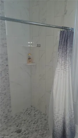 Shower stall with floor-to-ceiling white and gray veined tile, mosaic tile shower pan, and built-in corner shelving