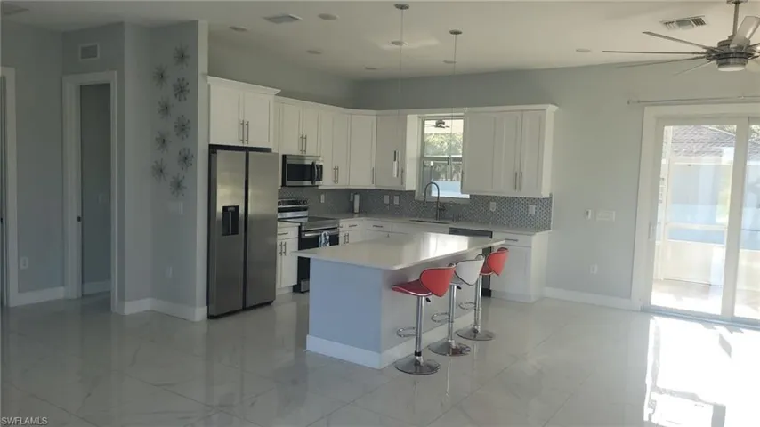 Spacious kitchen featuring white cabinetry, stainless steel appliances, a center island with countertop seating, a mosaic tile backsplash, and large format tile flooring