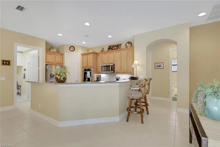 Kitchen with arched walkways, light brown cabinetry, recessed lighting, stainless steel appliances, and decorative backsplash