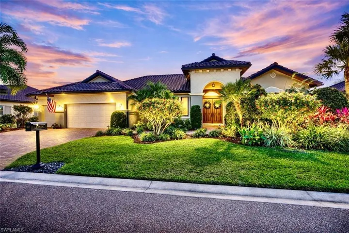 The property features a well-maintained lawn, lush landscaping, and a paver driveway