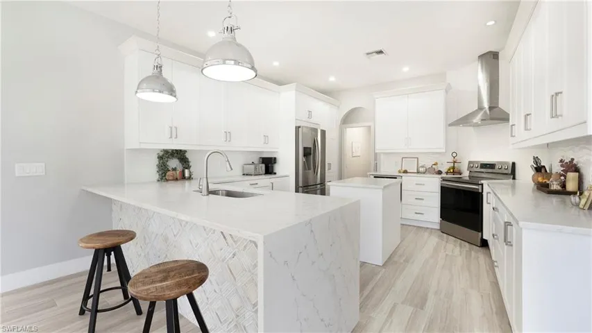 Kitchen with a center island, a kitchen bar, appliances with stainless steel finishes, wall chimney range hood, and a peninsula