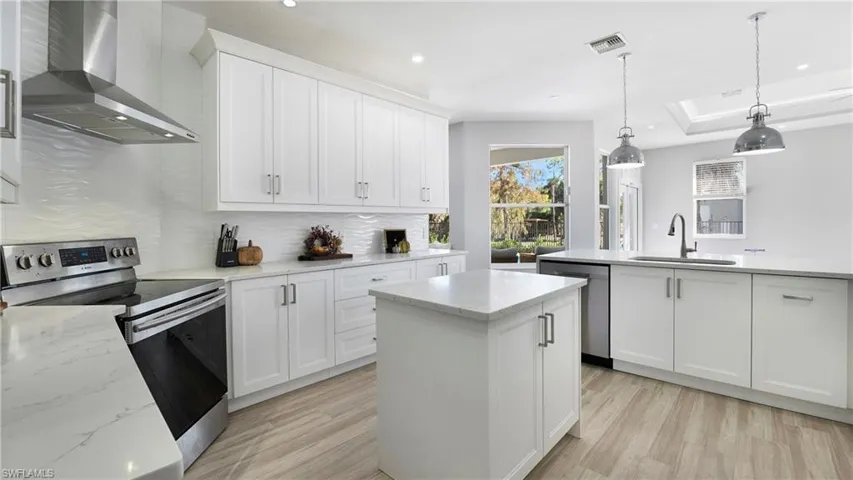 Kitchen featuring stainless steel appliances, wall chimney exhaust hood, a kitchen island, decorative light fixtures, and white cabinetry