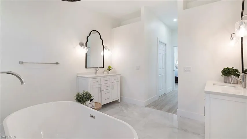 Full bathroom with a freestanding tub, light marble finish floors, and two vanities