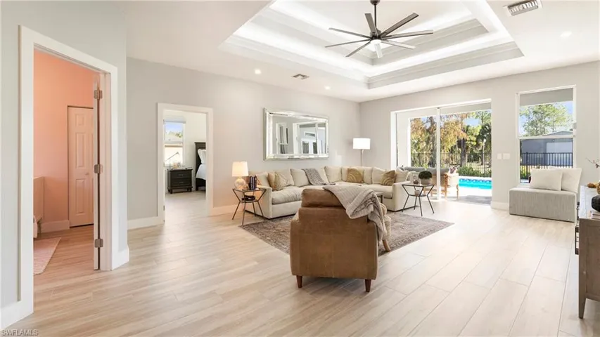 Living room featuring ornamental molding, a ceiling fan, light wood finished floors, recessed lighting, and a raised ceiling