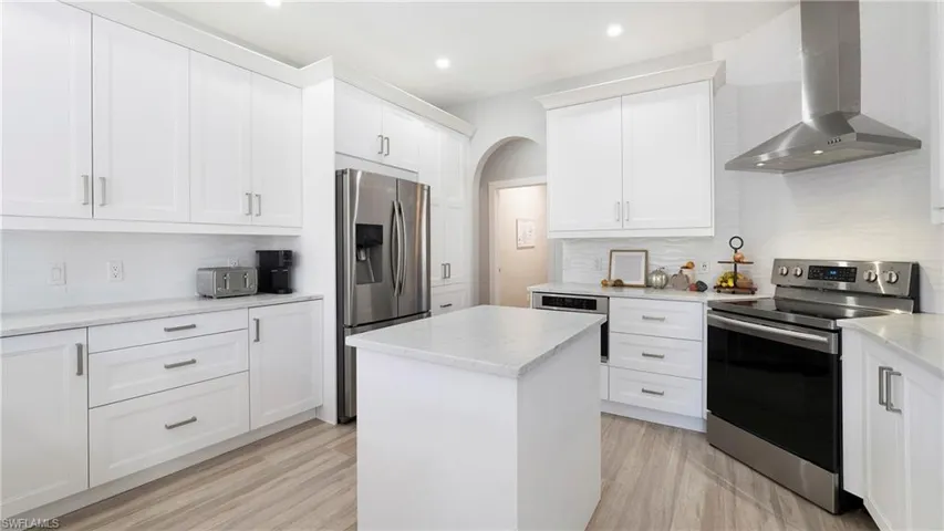 Kitchen featuring stainless steel appliances, wall chimney range hood, decorative backsplash, a center island, and white cabinetry