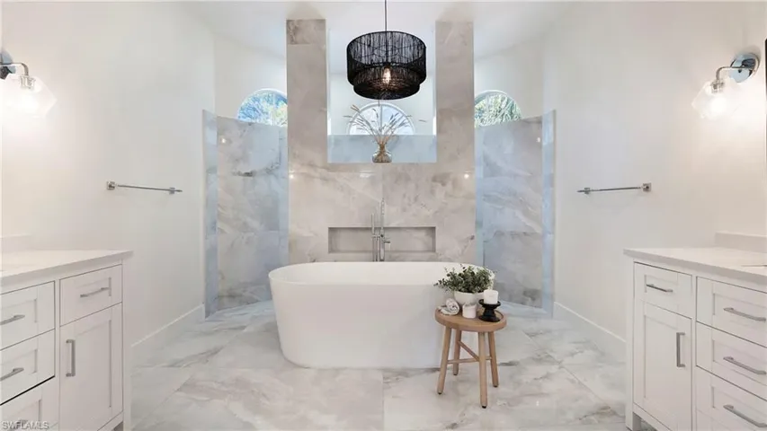 Bathroom featuring vanity, a soaking tub, light marble finish floors, and plenty of natural light