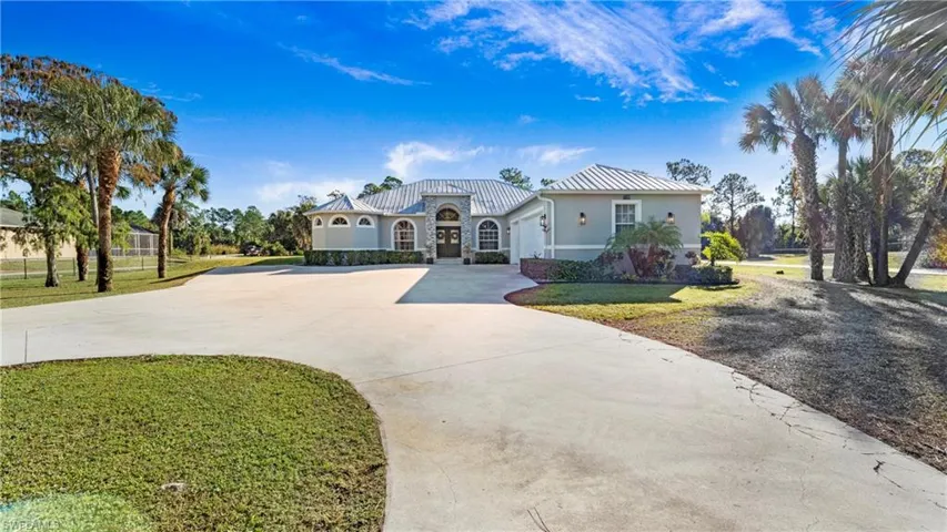 Mediterranean / spanish-style home with driveway, stucco siding, a front lawn, stone siding, and a metal roof