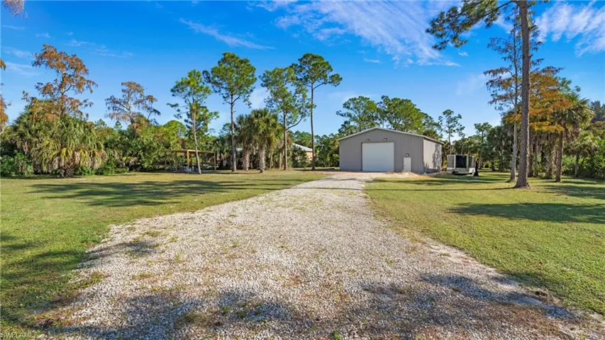 View of green lawn featuring a garage, gravel driveway, and an outbuilding