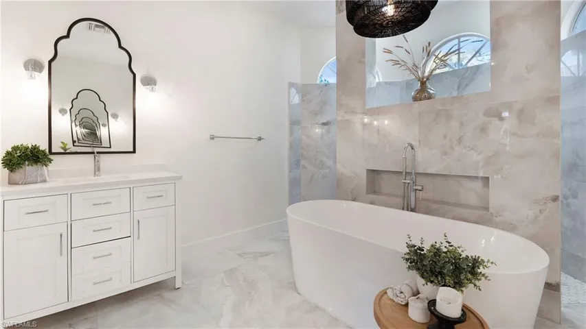 Bathroom featuring light marble finish flooring, vanity, and a freestanding tub