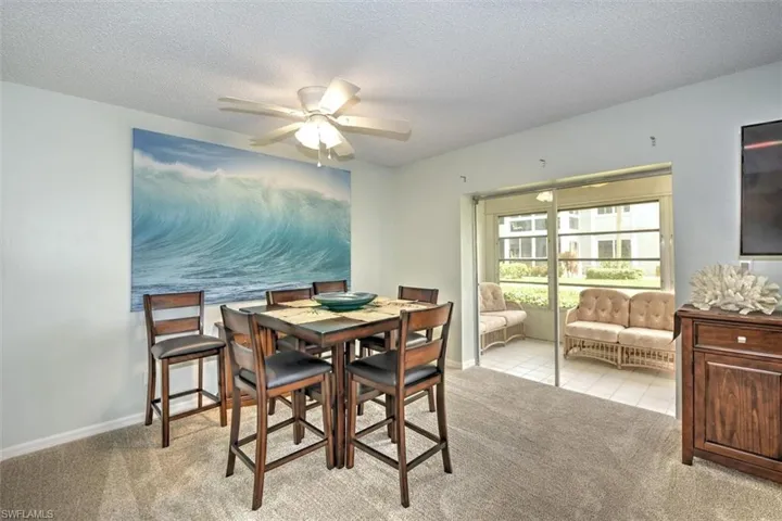 Carpeted interior dining space featuring a ceiling fan with integrated lighting, a wood-finish dining table, and direct access to a screened patio with tiled flooring