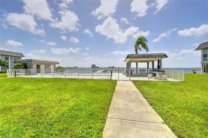 Expansive green space featuring a concrete pathway leading to a fenced pool area with a covered gazebo