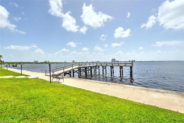 Waterfront pier with wood railings and structural supports, bordered by a concrete walkway