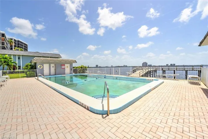 Outdoor swimming pool surrounded by a paver deck, with a waterfront backdrop