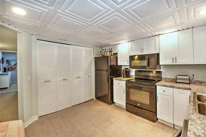 Kitchen featuring white shaker-style cabinetry, black appliances, textured countertops, and tile flooring