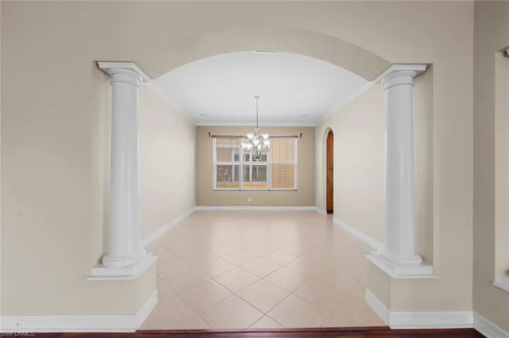 Unfurnished dining area with a chandelier, ornate columns, arched walkways, light tile patterned flooring, and ornamental molding