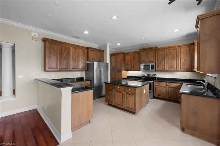 Kitchen featuring ornamental molding, stainless steel appliances, a kitchen island, recessed lighting, and dark stone counters
