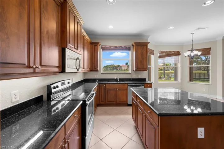 Kitchen featuring stainless steel appliances, dark stone counters, pendant lighting, crown molding, and a kitchen island