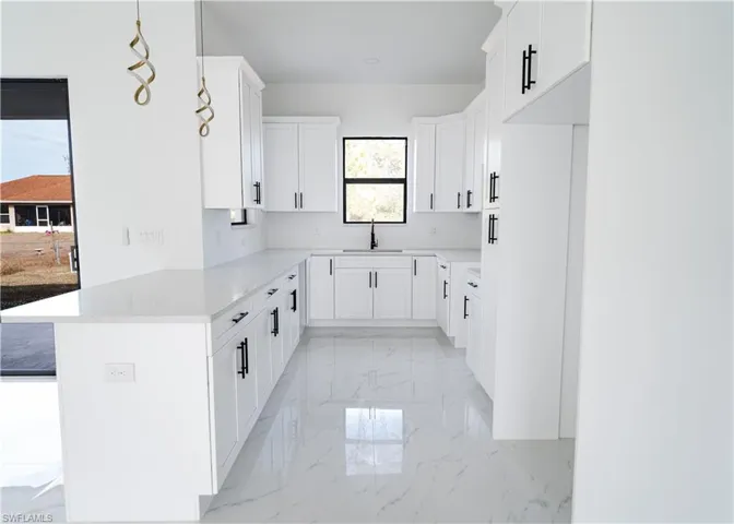 Kitchen with light marble finish floors, white cabinets, light stone countertops, and a peninsula