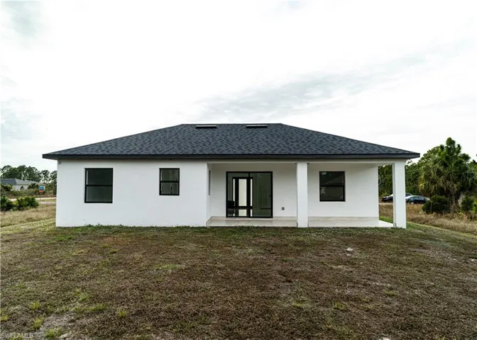 Rear view of property with stucco siding, a lawn, a patio, and a shingled roof