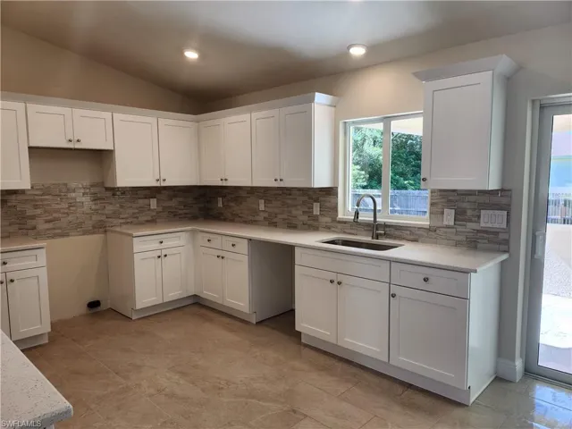 Kitchen featuring white cabinetry, light stone counters, tasteful backsplash, lofted ceiling, and recessed lighting