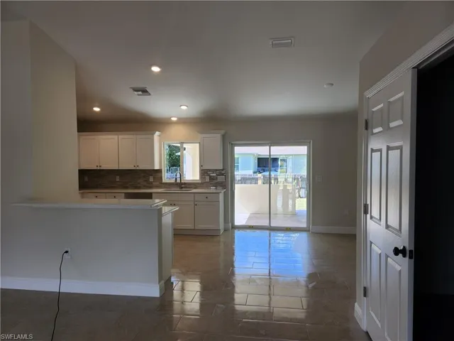 Kitchen featuring tasteful backsplash, white cabinetry, recessed lighting, light stone counters, and dark tile patterned floors