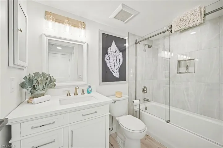 Full bathroom with enclosed tub/shower combo, vanity, and light vinyl wood-style floors
