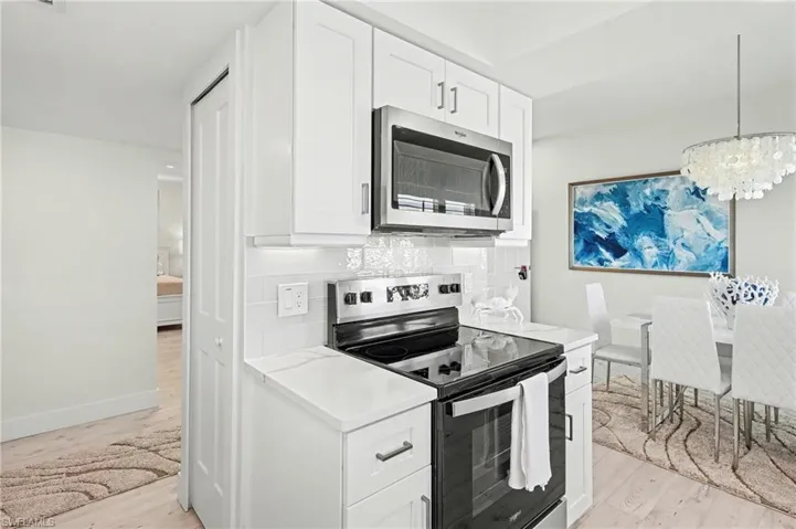 Kitchen with appliances with stainless steel finishes, white cabinetry, tasteful backsplash, light vinyl tile finished floors, and hanging light fixtures