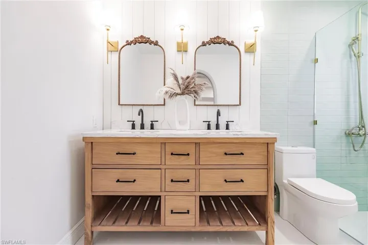Bathroom featuring a shower with shower door, toilet, oversized vanity, and dual sinks