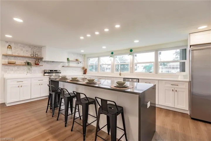 Kitchen with light hardwood / wood-style flooring, tasteful backsplash, stainless steel appliances, white cabinets, and a breakfast bar area