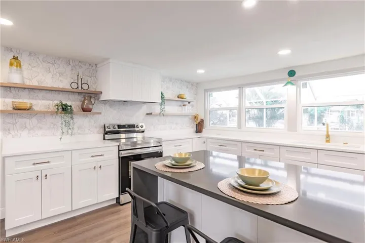 Kitchen featuring light hardwood / wood-style floors, range with electric cooktop, backsplash, sink, and white cabinets