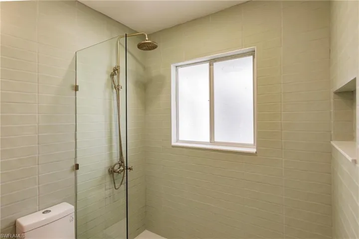 Bathroom featuring tiled shower, toilet, and tile walls