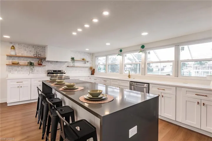 Kitchen with light hardwood / wood-style floors, white cabinetry, a kitchen island, appliances with stainless steel finishes, and backsplash