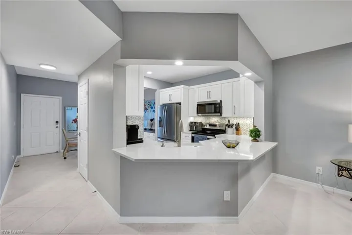 Kitchen with appliances with stainless steel finishes, backsplash, light tile patterned floors, lofted ceiling, and white cabinetry