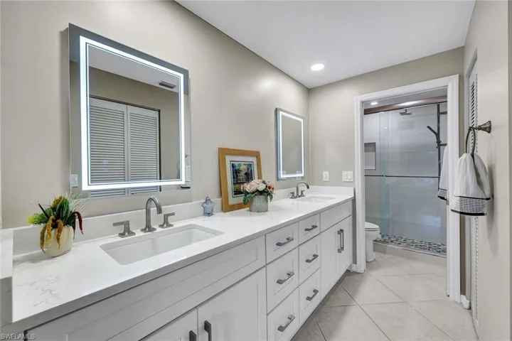 Bathroom featuring dual vanity, toilet, tile patterned floors, and walk in shower