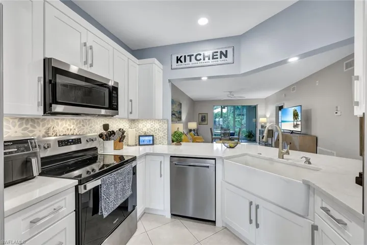Kitchen with white cabinetry, stainless steel appliances, kitchen peninsula, sink, and light tile patterned floors