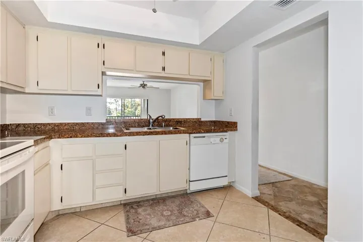 Kitchen featuring white appliances, cream cabinetry, a ceiling fan, a tray ceiling, and light tile patterned flooring