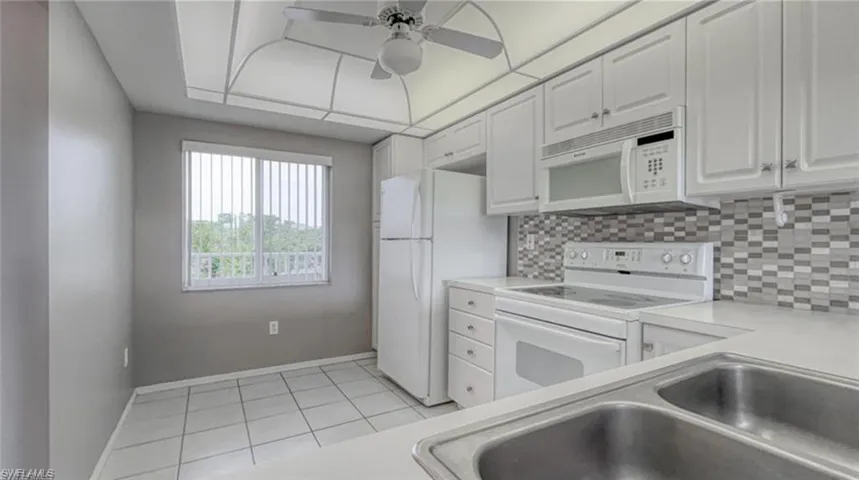 Kitchen featuring decorative backsplash, white appliances, sink, white cabinetry, and light tile patterned flooring