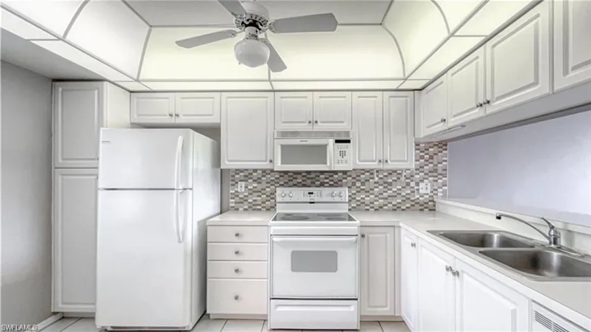 Kitchen with white cabinets, white appliances, sink, and light tile patterned floors